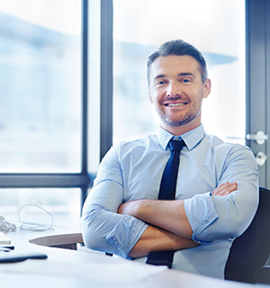 Portrait of a smiling businessman sitting at his desk with his arms crossed