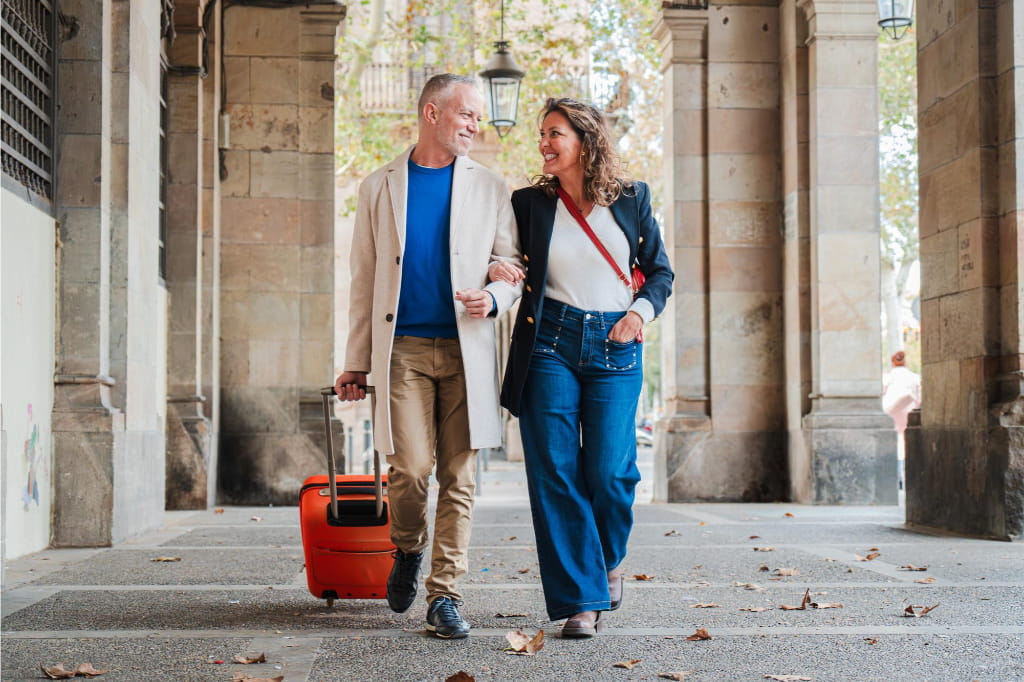 Pareja de mediana edad sonriendo y caminando bajo unos arcos de piedra durante un viaje.