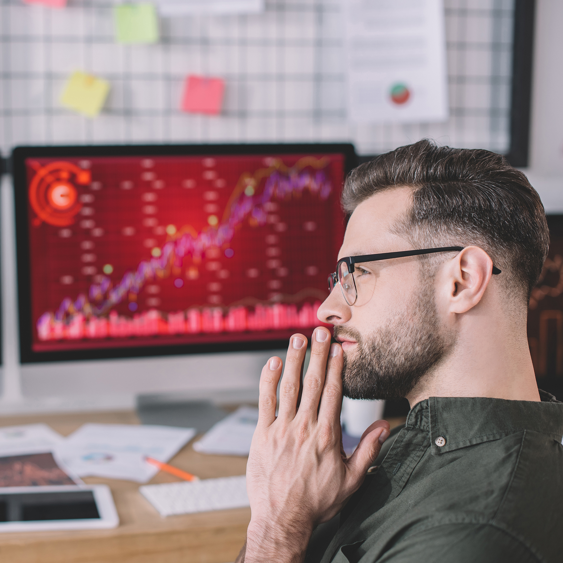 Side view of thoughtful computer system analyst looking away near digital devices on table